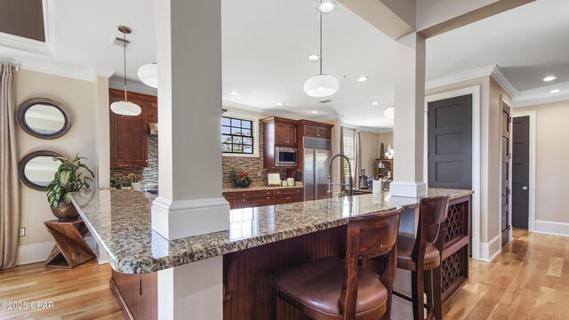 kitchen with tasteful backsplash, stone countertops, hanging light fixtures, stainless steel microwave, and kitchen peninsula