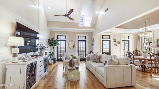 living room featuring ceiling fan with notable chandelier, a towering ceiling, ornamental molding, and light hardwood / wood-style floors