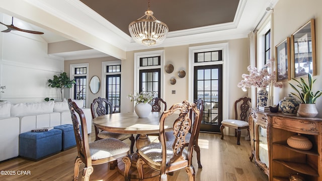 dining space with crown molding, wood-type flooring, a raised ceiling, and ceiling fan with notable chandelier