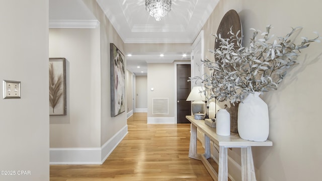 corridor with wood-type flooring, ornamental molding, an inviting chandelier, and a tray ceiling