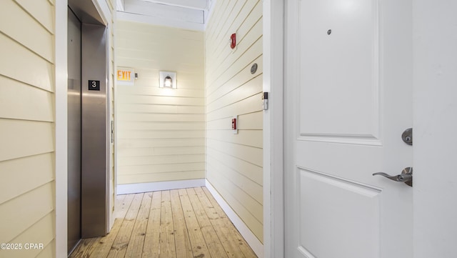 corridor with elevator, light hardwood / wood-style floors, and wood walls