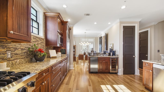 kitchen with light stone counters, hanging light fixtures, light wood-type flooring, stainless steel appliances, and beverage cooler