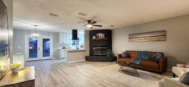 living area featuring a textured ceiling, a stone fireplace, visible vents, and light wood-style floors