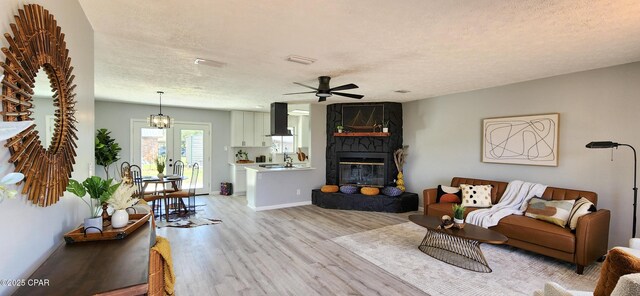 unfurnished living room featuring ceiling fan, a fireplace, light hardwood / wood-style floors, a textured ceiling, and french doors