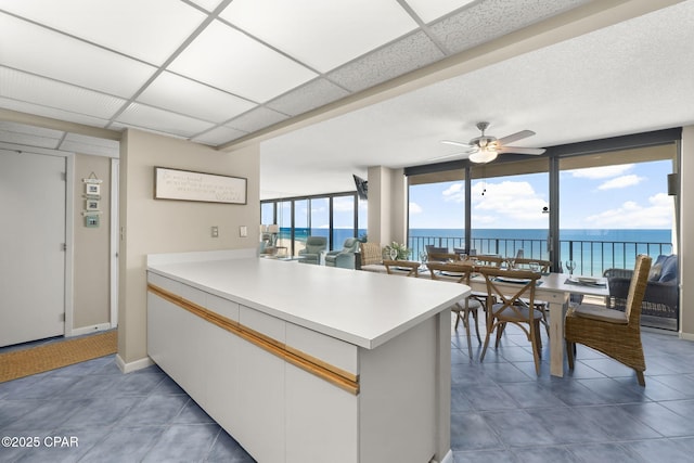 kitchen with floor to ceiling windows, a water view, a paneled ceiling, kitchen peninsula, and white cabinets