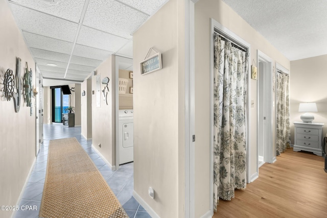 hall featuring washer / clothes dryer, light tile patterned floors, and a drop ceiling