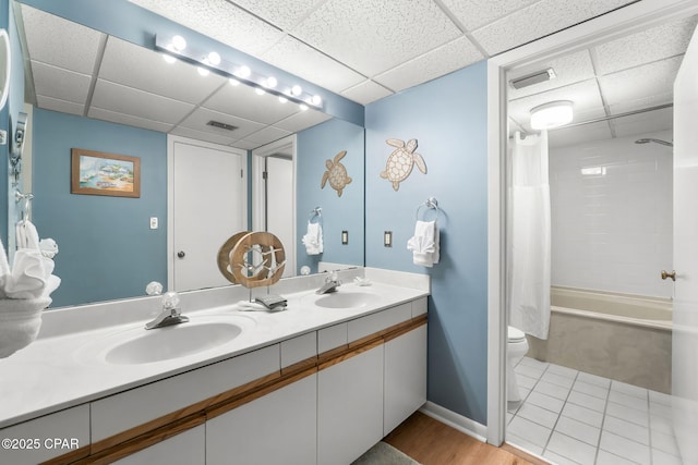 full bathroom featuring vanity, a drop ceiling, shower / bathtub combination with curtain, and toilet