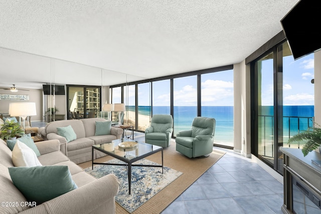 tiled living room with a water view, ceiling fan, expansive windows, and a textured ceiling