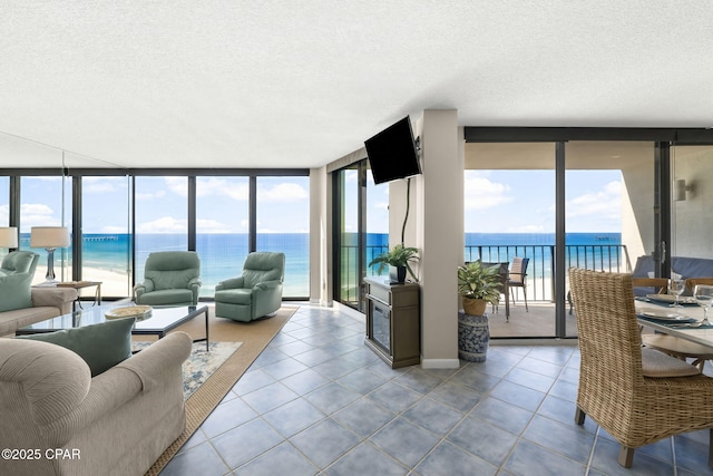 living room featuring expansive windows, light tile patterned floors, a water view, a healthy amount of sunlight, and a beach view