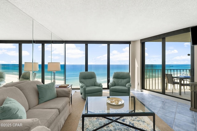 living room with a view of the beach, a wall of windows, a water view, tile patterned floors, and a textured ceiling