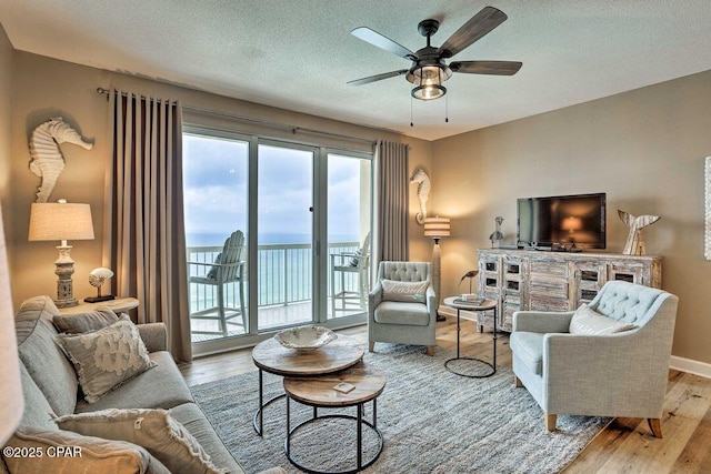 living room with ceiling fan, light hardwood / wood-style flooring, and a textured ceiling