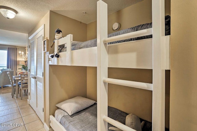 bedroom featuring an inviting chandelier, a closet, a textured ceiling, and light tile patterned floors