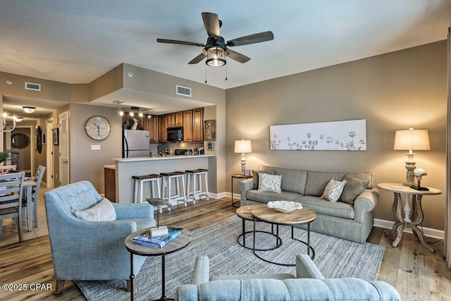 living room with a textured ceiling, ceiling fan, and light wood-type flooring