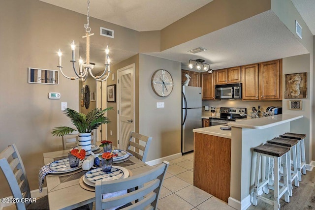 kitchen with light tile patterned flooring, a chandelier, appliances with stainless steel finishes, a kitchen breakfast bar, and kitchen peninsula