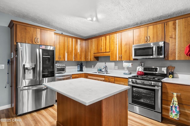 kitchen with brown cabinetry, light wood-style flooring, stainless steel appliances, light countertops, and a sink