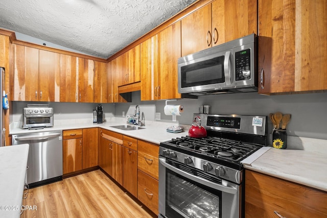 kitchen featuring light wood finished floors, light countertops, appliances with stainless steel finishes, a sink, and a textured ceiling