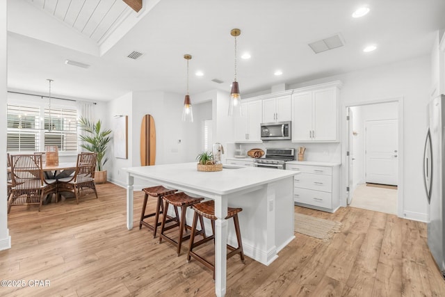 kitchen with pendant lighting, light hardwood / wood-style flooring, a kitchen island with sink, stainless steel appliances, and white cabinets