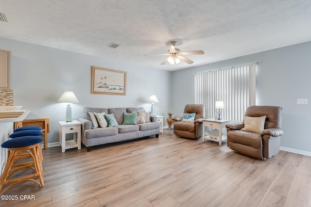 living room with ceiling fan, a textured ceiling, and light wood-type flooring