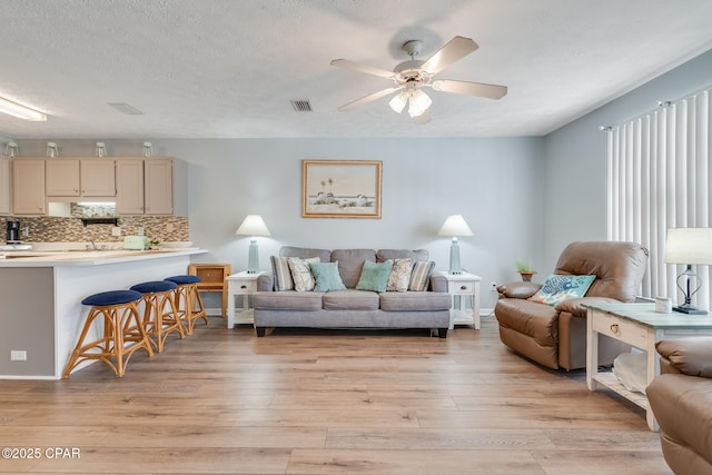 living room with ceiling fan, light hardwood / wood-style flooring, and a textured ceiling