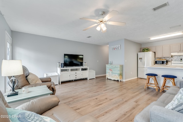 living room with ceiling fan, a textured ceiling, and light wood-type flooring