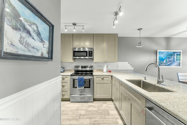 kitchen featuring sink, hanging light fixtures, stainless steel appliances, light stone counters, and track lighting