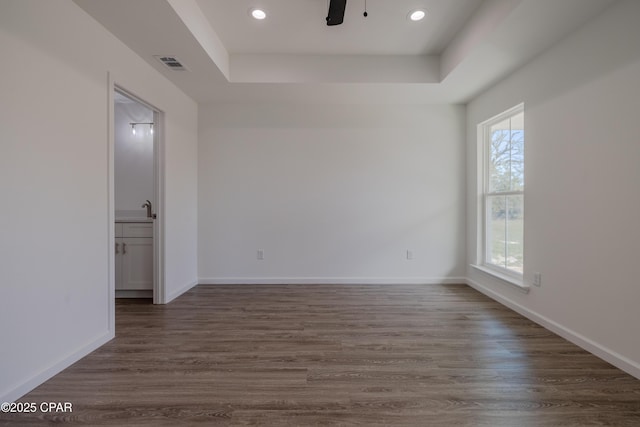 spare room featuring dark wood-style floors, a tray ceiling, visible vents, a sink, and baseboards