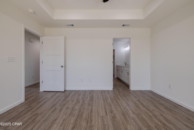 unfurnished bedroom with light wood-type flooring, a raised ceiling, and visible vents