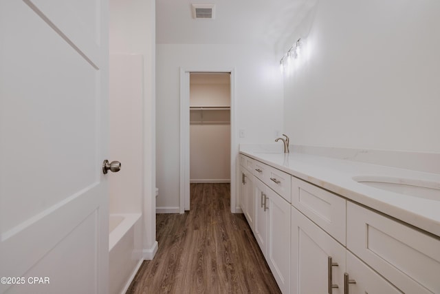 bathroom with a washtub, double vanity, visible vents, a sink, and wood finished floors