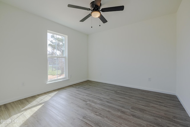 empty room featuring dark wood-type flooring, a wealth of natural light, ceiling fan, and baseboards