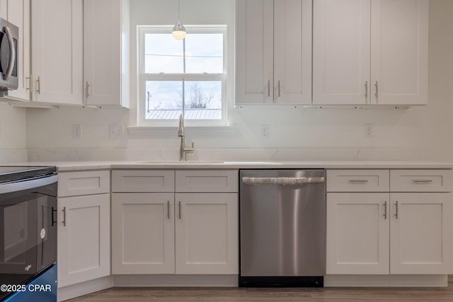 kitchen featuring pendant lighting, appliances with stainless steel finishes, a sink, and white cabinets