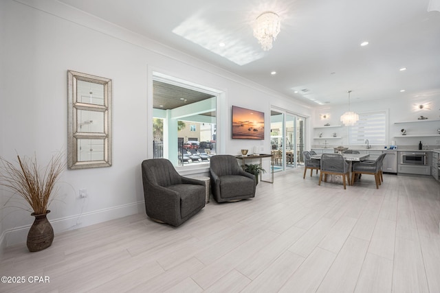 living room with ornamental molding, sink, a chandelier, and light hardwood / wood-style floors
