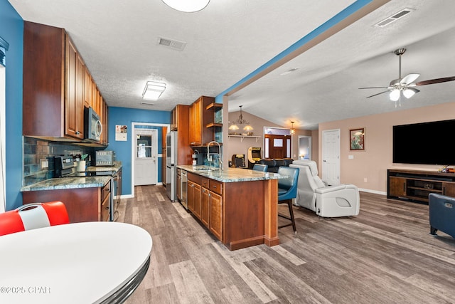 kitchen featuring brown cabinets, visible vents, appliances with stainless steel finishes, open floor plan, and a sink