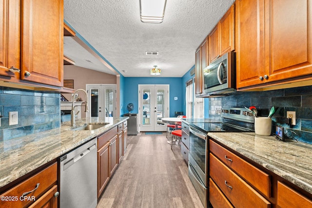 kitchen with french doors, stainless steel appliances, visible vents, brown cabinetry, and light stone countertops