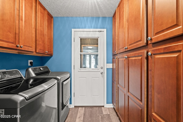 washroom featuring a textured ceiling, baseboards, cabinet space, light wood finished floors, and washing machine and clothes dryer