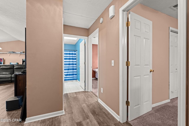 corridor with baseboards, a textured ceiling, and wood finished floors