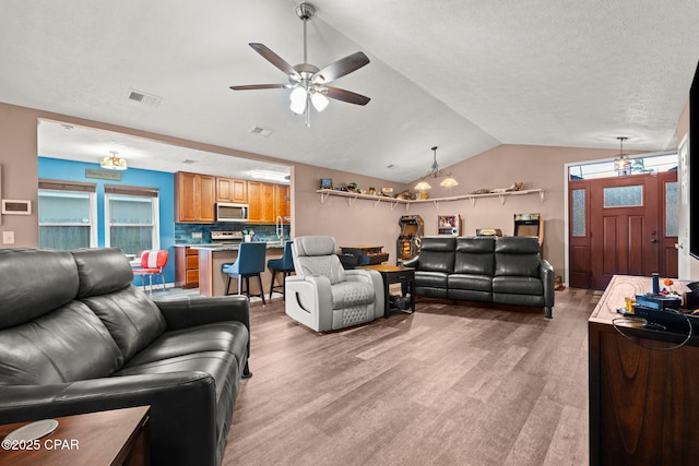 living area featuring lofted ceiling, light wood-type flooring, visible vents, and a ceiling fan