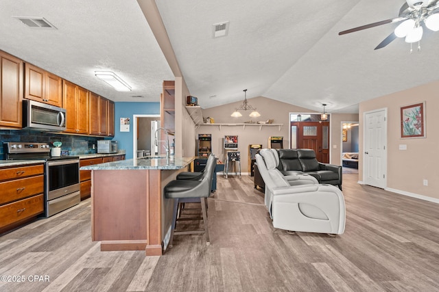 kitchen with stainless steel appliances, a kitchen breakfast bar, hanging light fixtures, backsplash, and a center island with sink