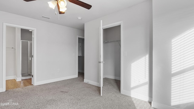 unfurnished bedroom with carpet floors, a walk in closet, a closet, visible vents, and baseboards