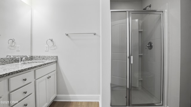 bathroom with a stall shower, vanity, baseboards, and wood finished floors