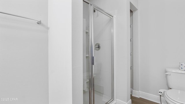 full bath featuring wood finished floors, a shower stall, toilet, and baseboards