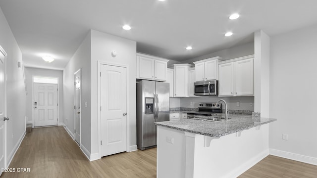 kitchen with light stone counters, appliances with stainless steel finishes, white cabinetry, light wood-type flooring, and a peninsula