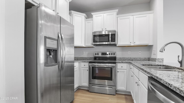 kitchen featuring appliances with stainless steel finishes, light stone counters, light wood-style floors, white cabinetry, and a sink