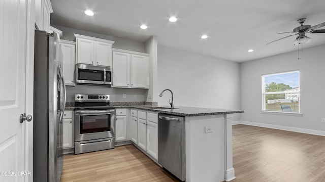 kitchen with a peninsula, a sink, white cabinetry, appliances with stainless steel finishes, and light wood-type flooring