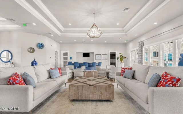 living room featuring a notable chandelier, ornamental molding, a raised ceiling, and light wood-type flooring