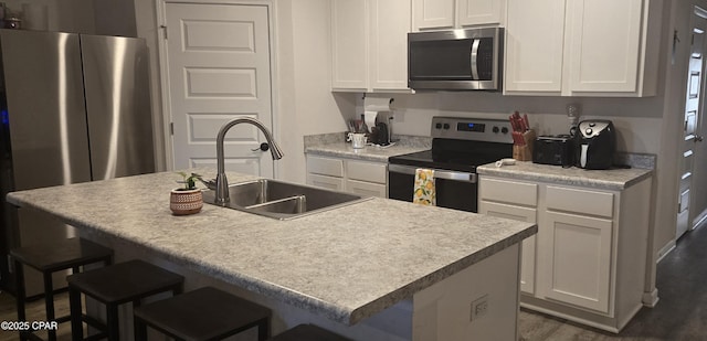 kitchen with white cabinetry, sink, stainless steel appliances, and an island with sink