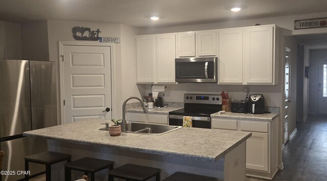 kitchen with sink, appliances with stainless steel finishes, an island with sink, white cabinets, and a kitchen bar