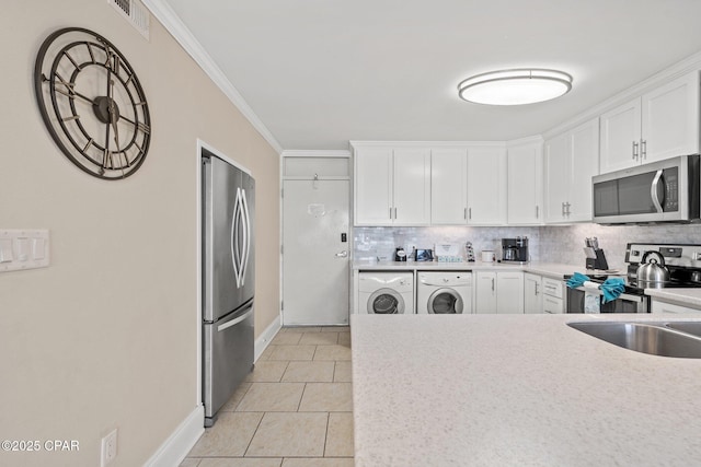 kitchen with stainless steel appliances, washing machine and dryer, white cabinets, and light countertops