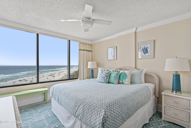 bedroom featuring a textured ceiling, a view of the beach, a water view, a ceiling fan, and ornamental molding