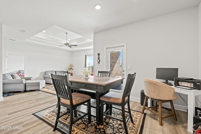 dining area featuring a tray ceiling, ceiling fan, and light hardwood / wood-style floors