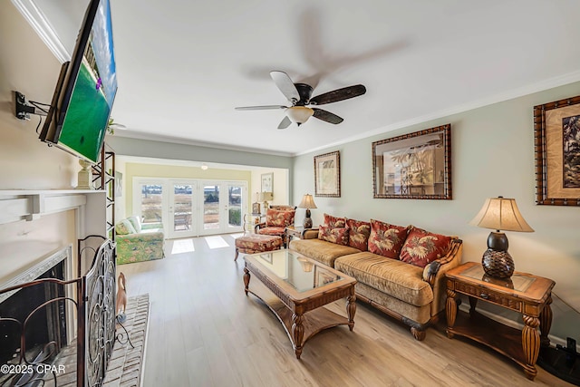 living room with ceiling fan, crown molding, a brick fireplace, light wood-type flooring, and french doors